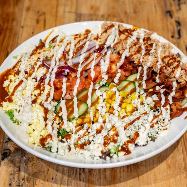 A large BBQ salad with pulled pork, bacon, corn, tomatoes, and blue cheese on a white plate.