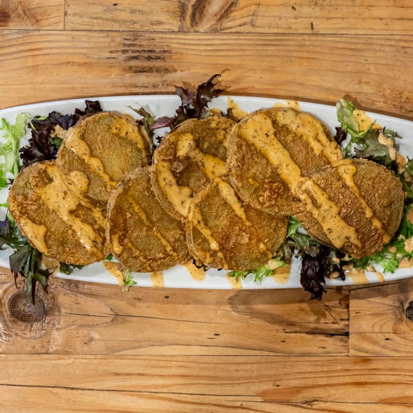 Fried green tomatoes with a creamy sauce and mixed greens on a white platter.