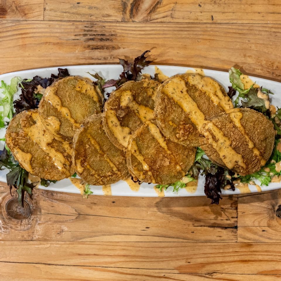 Fried green tomatoes with a creamy sauce and mixed greens on a white platter.