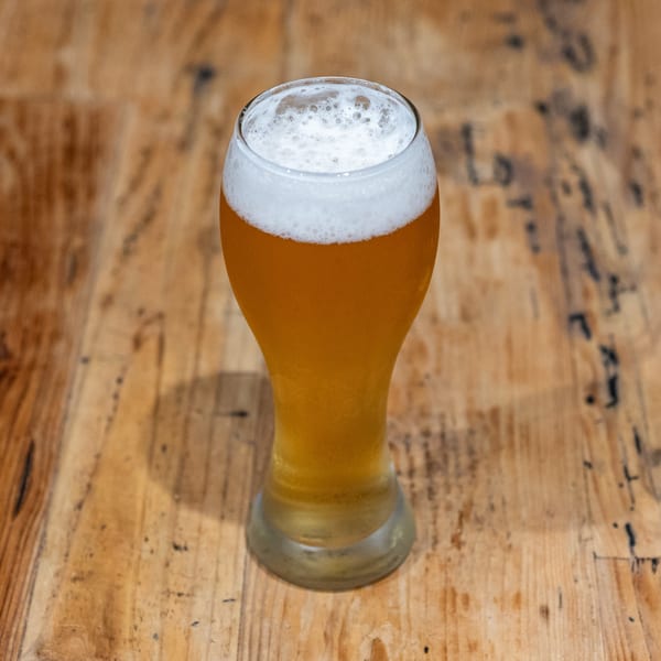 A tall glass of golden beer with a frothy white head sits on a rustic wooden table.