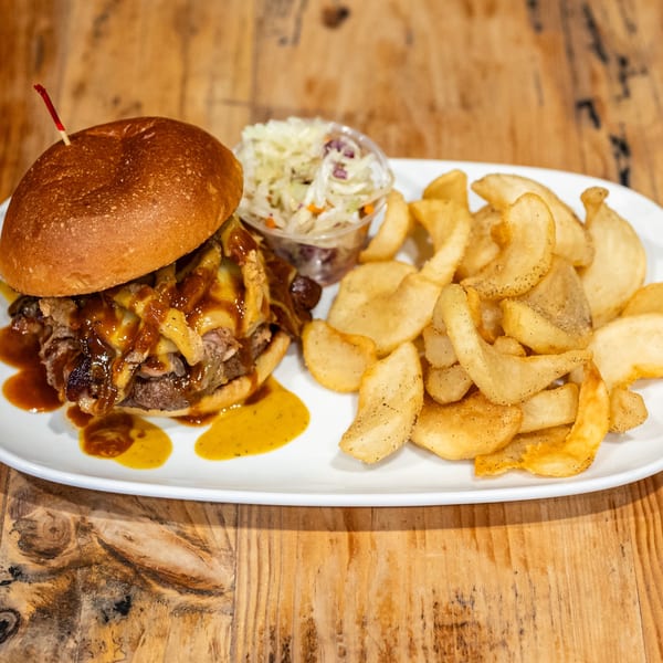 BBQ pulled pork sandwich with melted cheese, crispy onions, fries, and coleslaw on a white plate.